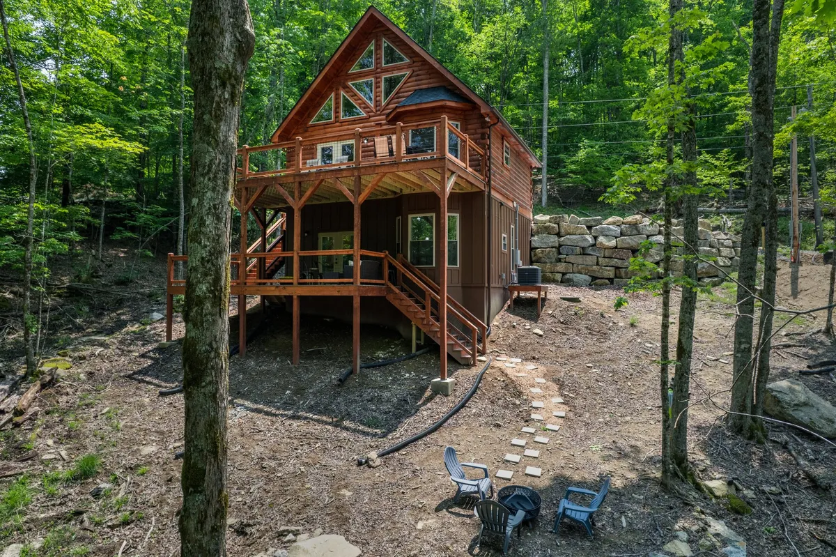 A wooden cabin surrounded by mature trees features an inviting outdoor seating area and a pathway that leads into the woods. The atmosphere is tranquil and ideal for family gatherings or a quiet morning coffee before heading out to explore the area.