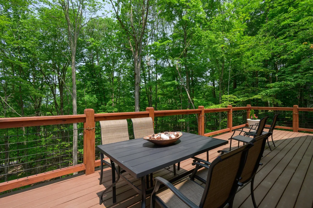 An inviting wooden deck nestled among trees, featuring a dining table and chairs. The scene conveys a sense of privacy and peacefulness, perfect for enjoying meals or morning coffee outdoors while immersed in nature.