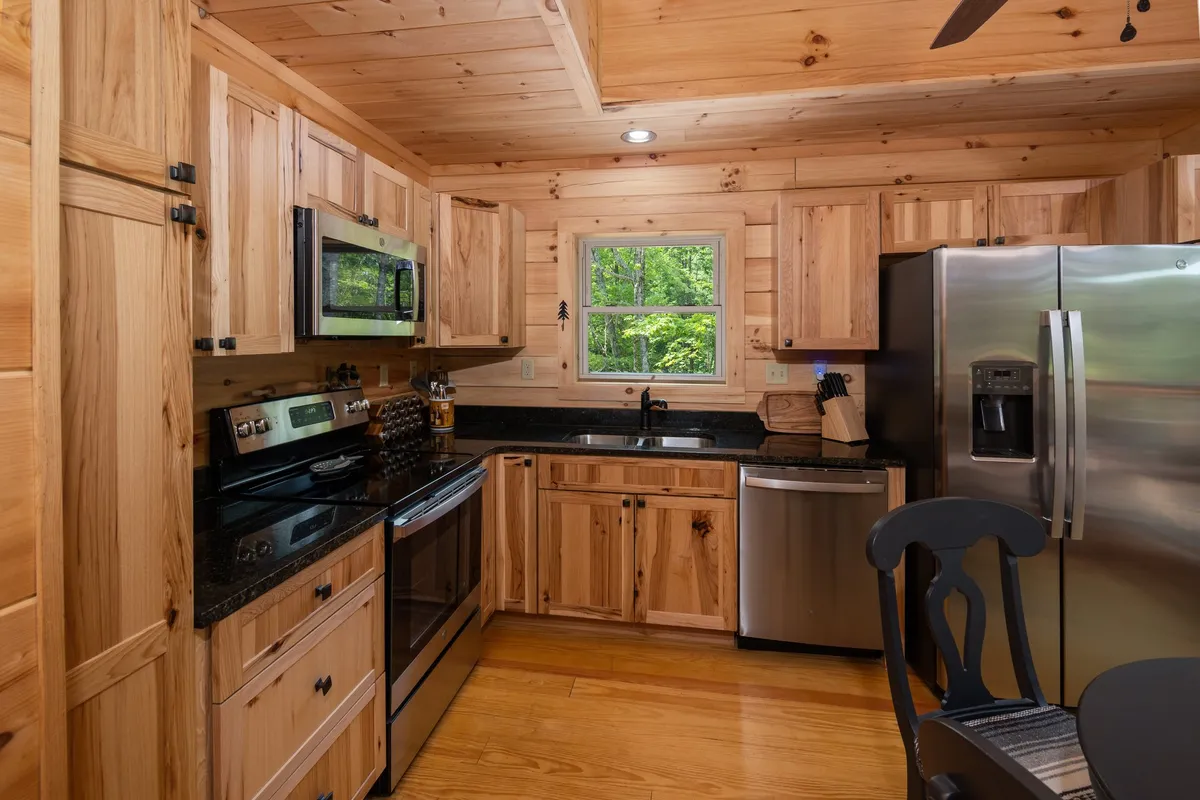 A close-up view of the kitchen area, highlighting modern stainless steel appliances, granite countertops, wooden cabinetry, and a window view that brings in natural light. The Keurig coffee maker and other amenities are subtly visible, emphasizing convenience and modernity.
