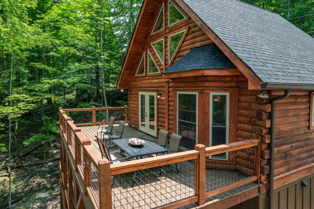 A cozy log cabin with a spacious deck furnished for outdoor dining and relaxation, set within verdant greenery. The inviting outdoor space hints at evening gatherings, stargazing, and recounting adventures after a day on the trails.