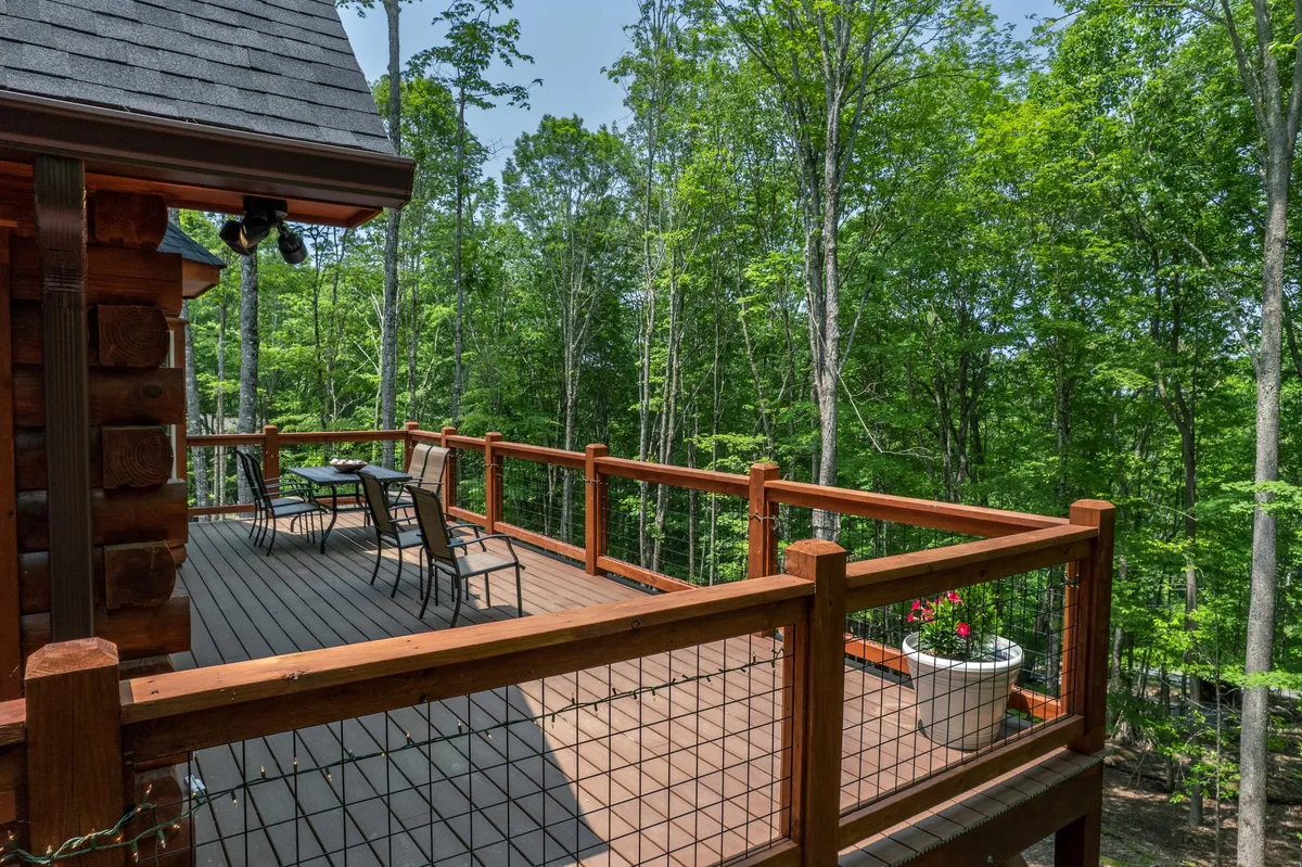 A serene wooden deck featuring comfortable outdoor chairs and a flower pot, surrounded by lush trees. The tranquil ambiance is ideal for relaxing with a book, enjoying sunrise views, or taking in the fresh woodland air.