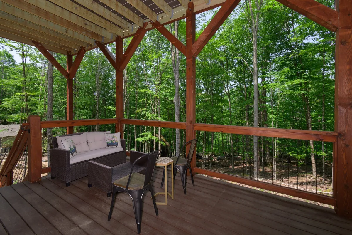 An outdoor seating area surrounded by mature trees, featuring comfortable chairs and a wooden railing. The tranquil atmosphere is ideal for relaxing, storytelling, and enjoying nature as the sun sets or for stargazing later in the evening.