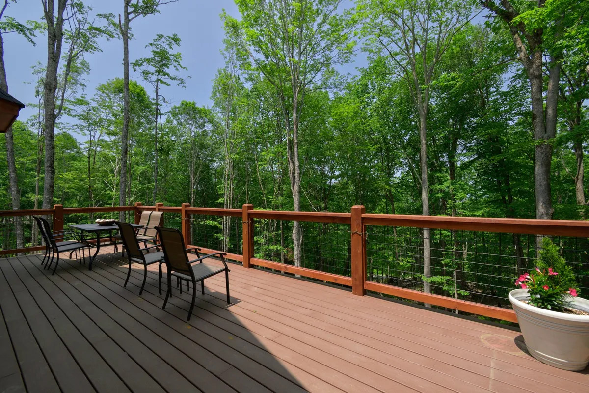 A wooden deck nestled among leafy trees, furnished with outdoor furniture suitable for small gatherings or quiet contemplation. The peaceful setting showcases the multiple outdoor spaces available for guests to enjoy the surrounding natural beauty and night sky.